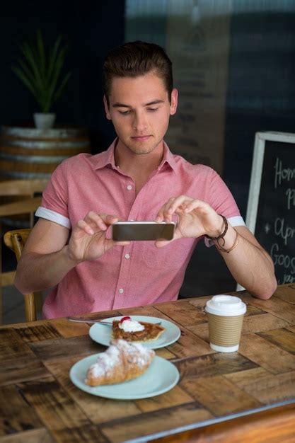 Premium Photo | Young man photographing food on table in coffee house