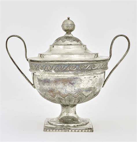 A silver sugar bowl with a lid and two fine handles decorated with ...