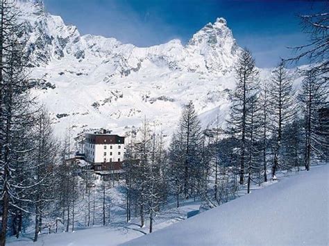 a snow covered mountain with a house in the foreground and trees on the other side