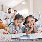 Little two girls drawing with colouring pencils lying on living room floor with their parents ...