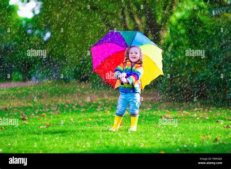 Child with colorful umbrella playing in the rain. Kids play outdoors by ...