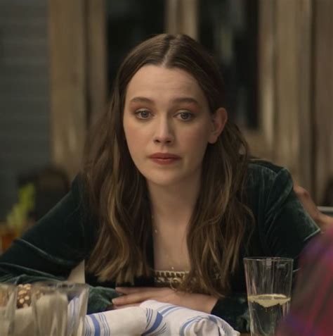 a woman sitting at a table with a glass of wine in front of her and another person behind her