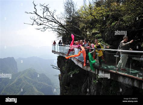 Tourists walk on the glass skywalk on the cliff of Tianmen Mountain (or Tianmenshan Mountain) in ...