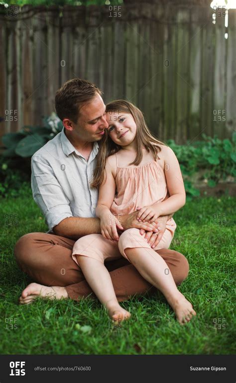 Daughter sitting on father's lap in backyard stock photo - OFFSET