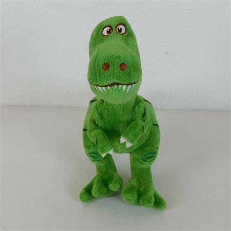 a green stuffed toy dinosaur with big eyes and sharp teeth, sitting on ...