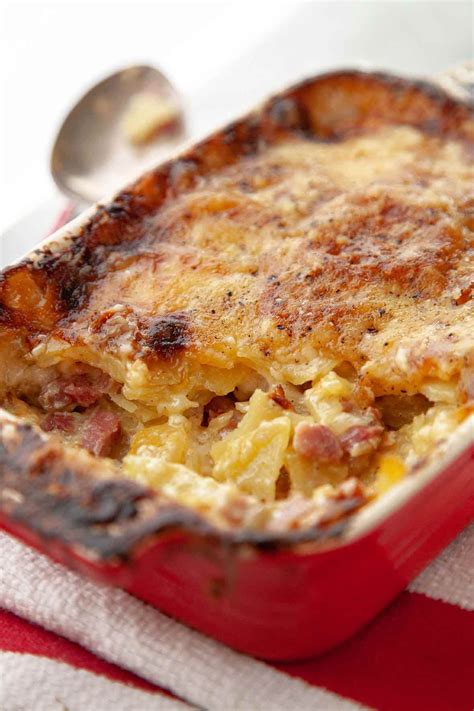 A red dish filled with a layered ham, cheese, and potato casserole on a red-and-white striped ...