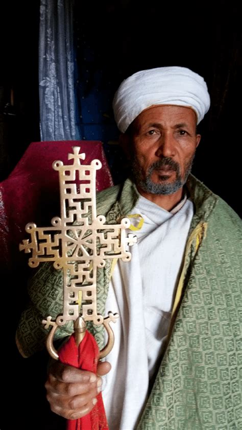 A priest holds one of the ancient crosses at Bete Maskel. The signs on ...