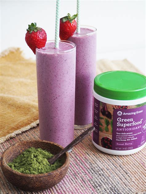 two smoothie cups with strawberries on top and green superfood next to them