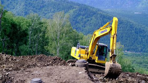 A yellow excavator works in the mountains. Construction of roads ...