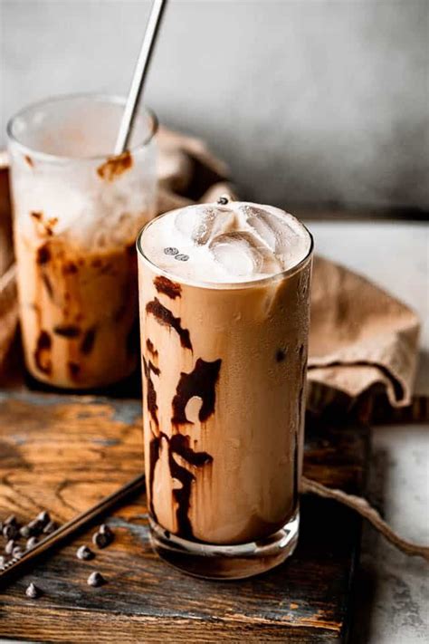 two glasses filled with iced coffee on top of a wooden table next to a ...