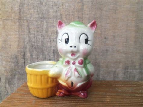 a ceramic cat sitting next to a yellow cup