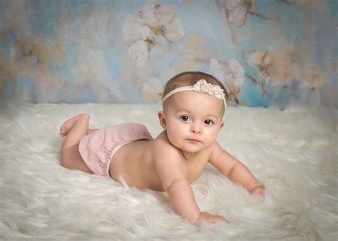 6 month old baby girl lying on white fur with headband on looking at ...