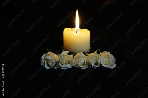 Beautiful White roses with a burning candle on the dark background. Funeral flower and candle on ...