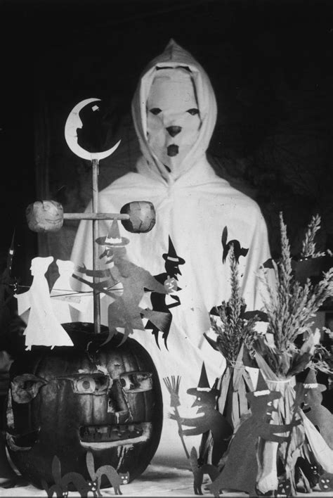 a black and white photo of a person dressed as a ghost next to pumpkins