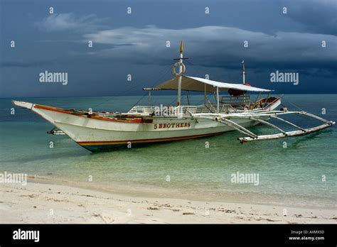 Bangka or traditional Philippino boat rests near shore while storm approaches Malapascua Island ...