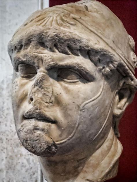 an ancient statue of a man's head is shown in front of a red wall