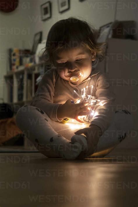 Cute baby girl holding christmas light while sitting at home stock photo