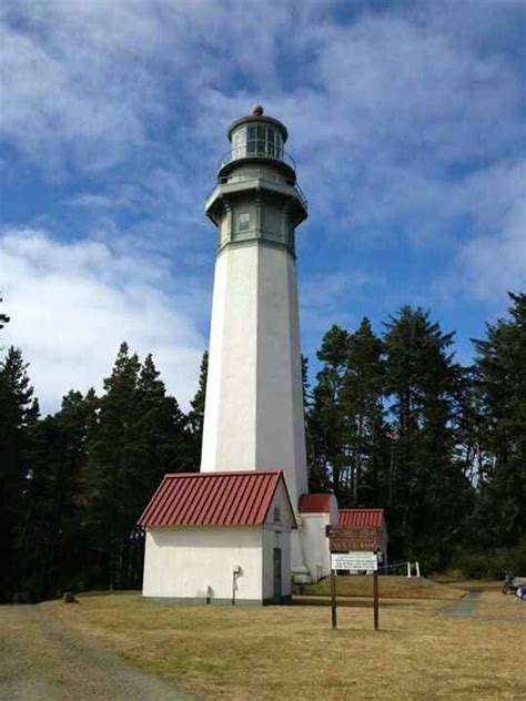 a white light house sitting on top of a grass covered field next to ...