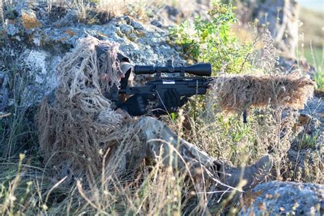 sniper in ghillie (camouflage) suit with a high-precision rifle with ...