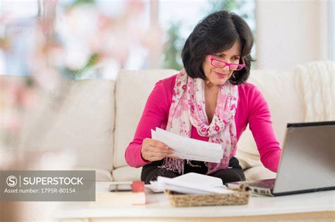 Portrait of senior woman sitting in living room with laptop - SuperStock