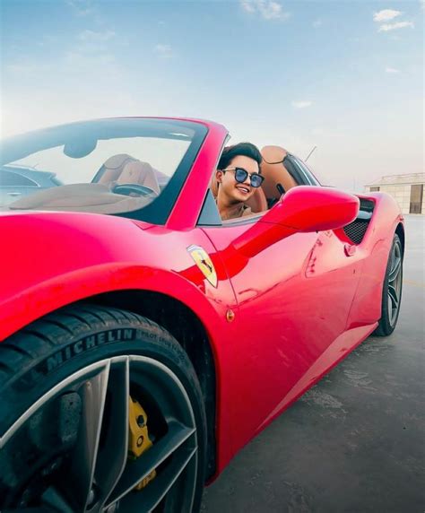 a man driving a red sports car on the beach with his head out the window