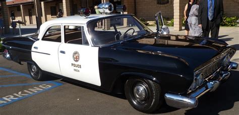 an old police car is parked in the parking lot with two men standing next to it