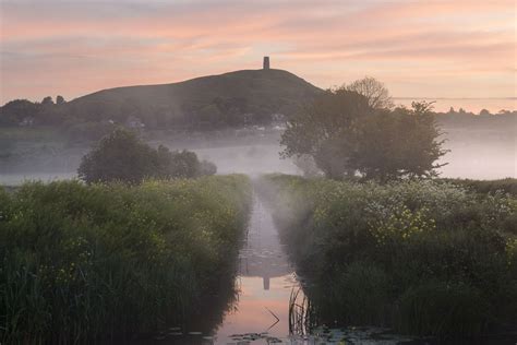 Mist shrouds Glastonbury Tor during a colourful spring sunrise on the Somerset Levels. Image ...