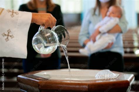 Priest pouring holy water into the baptismal font, moments before a child receives the sacrament ...