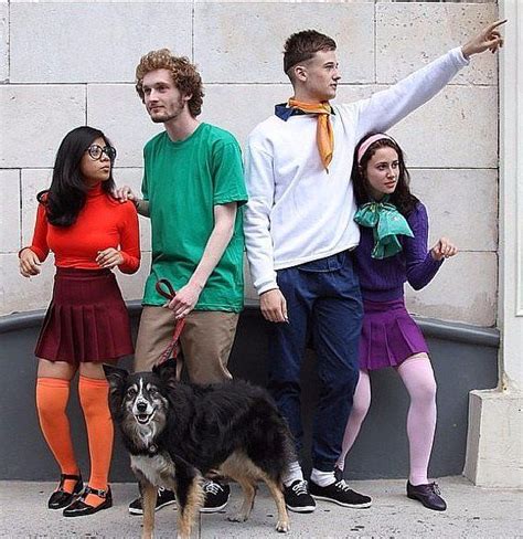 four people and a dog are standing in front of a building with their arms up