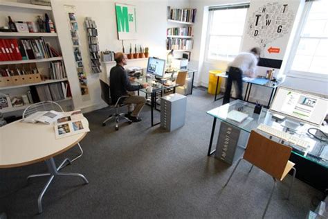 an office with two people working at their desks in front of bookshelves