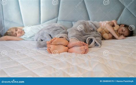 Two Barefoot Children Lie Side by Side Under a Blanket on a Large Bed ...