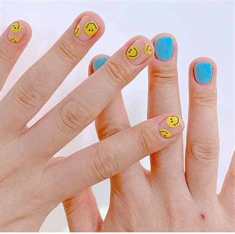 three fingers with smiley faces painted on them and one has blue fingernails, the other has yellow