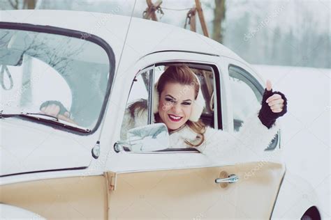 Young woman driving vintage car at snowy road. Happy caucasian woman driving a VW beetle car ...