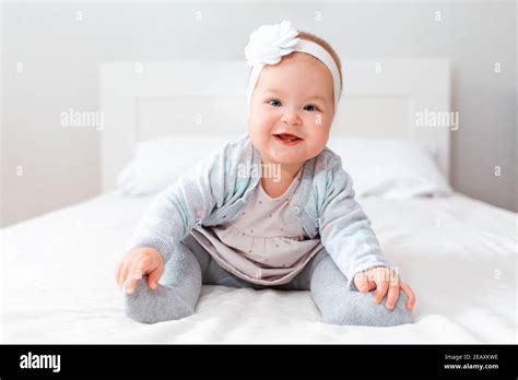 Funny smiling little girl in a dress and with a bandage on her head, sitting on the bed ...