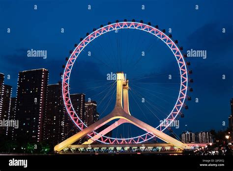 A night view of the Tianjin Eye with glowing lights on a background of modern buildings, Tianjin ...