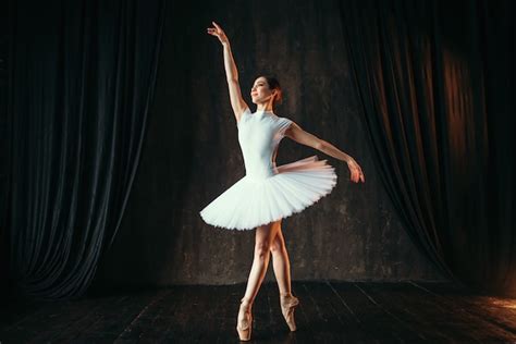 Bailarina de elegância em vestido branco e sapatilhas de ponta dançando no palco teatral ...