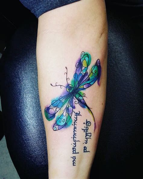 a colorful dragonfly tattoo on the right arm and leg with words written below it