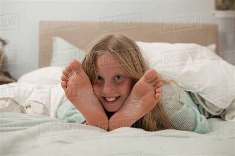 Portrait of girl lying on bed in between feet - Stock Photo - Dissolve