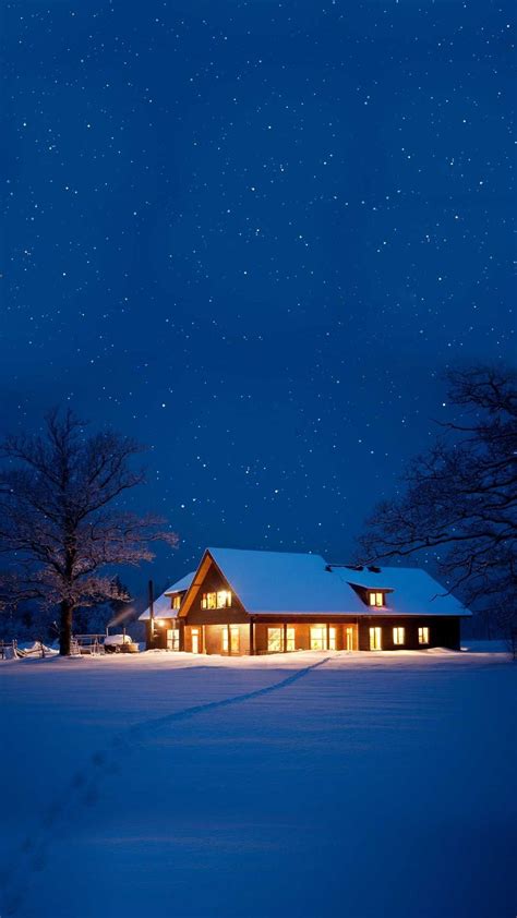 a house is lit up at night in the snow with stars above it and trees