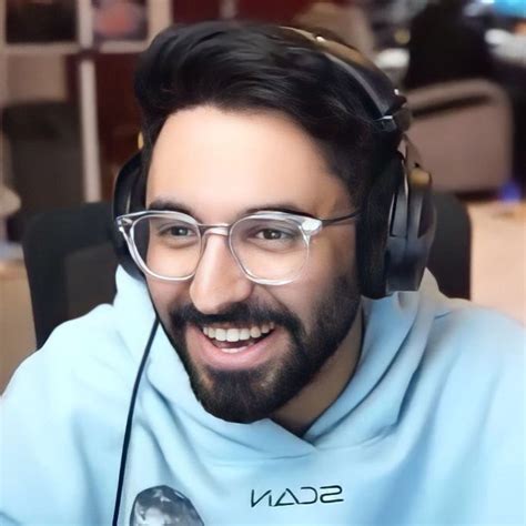 a man wearing glasses and headphones sitting in front of a computer monitor smiling at the camera