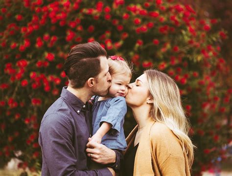 a man and woman are kissing their son in front of some red flowered trees