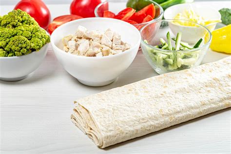 Fresh whole and sliced vegetables with chicken fillet and pita on the kitchen table (Flip 2019 ...
