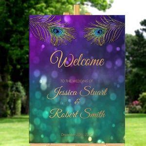 a welcome sign with a peacock feather on it in front of some grass and trees