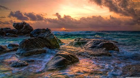 Download A Sunset Over The Ocean With Rocks And Water Wallpaper ...