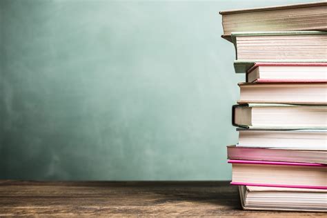 Textbooks stacked on school desk with chalkboard background. | GoodCities