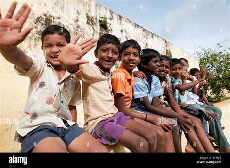 Rural Indian village boys sitting on a school wall waving in bright sunlight. Andhra Pradesh ...