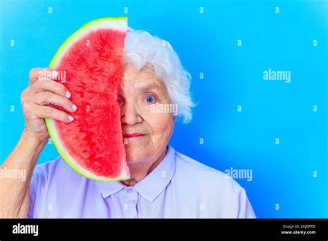 mature woman with snow white grey white hair in blue shirt holding watermelon in studio ...