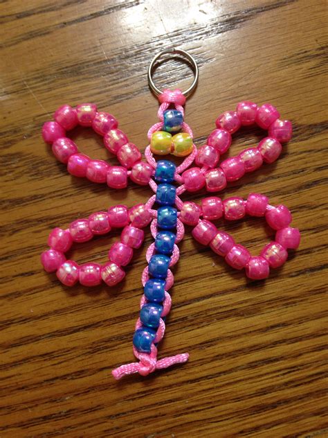 a pink and blue dragon keychain sitting on top of a wooden table with beads