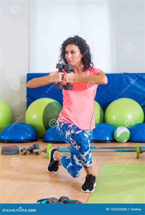 Fit Female Sportswoman Doing Curtsy Lunge Exercise with Dumbbells in Group Fitness Studio Class ...