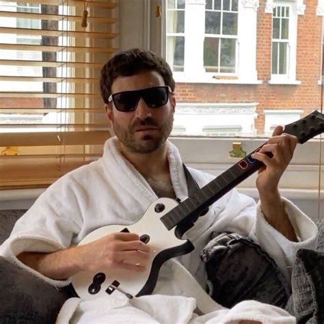 a man sitting on a couch holding an electric guitar in his right hand and wearing sunglasses